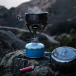 selective focus of blue and gray camping gas burner and cooking pan on cliff