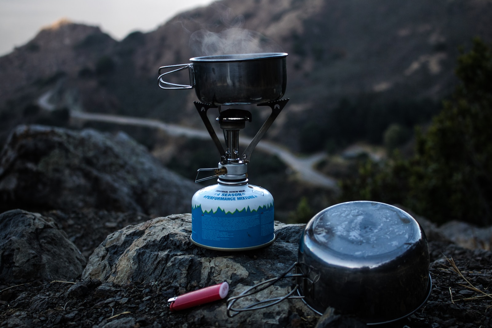 selective focus of blue and gray camping gas burner and cooking pan on cliff