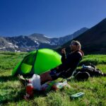 man sitting on black camping chair beside green dome tent
