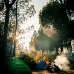 two persons sitting near two camping tents in the woods